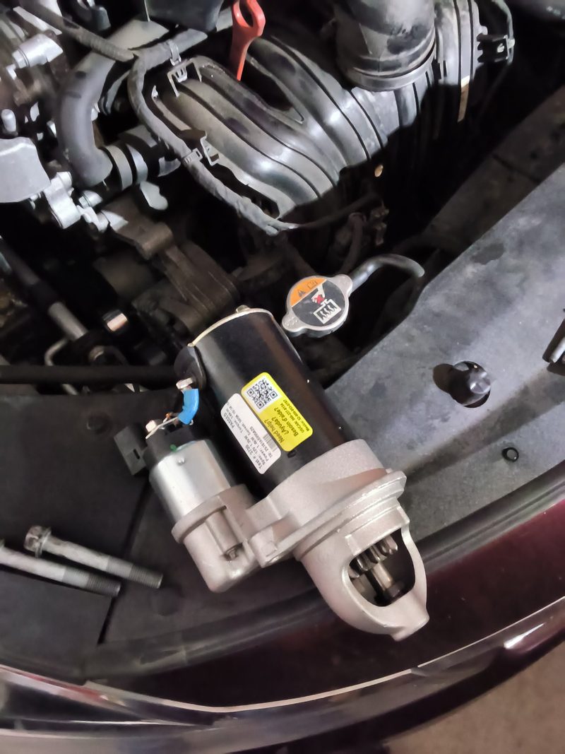 A replacement starter motor resting on the radiator support of the Kia Optima