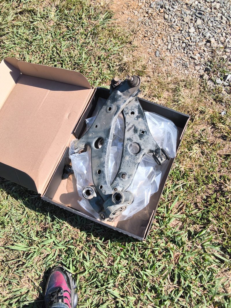 A removed lower control arm lying in the open box of the new part on the grass