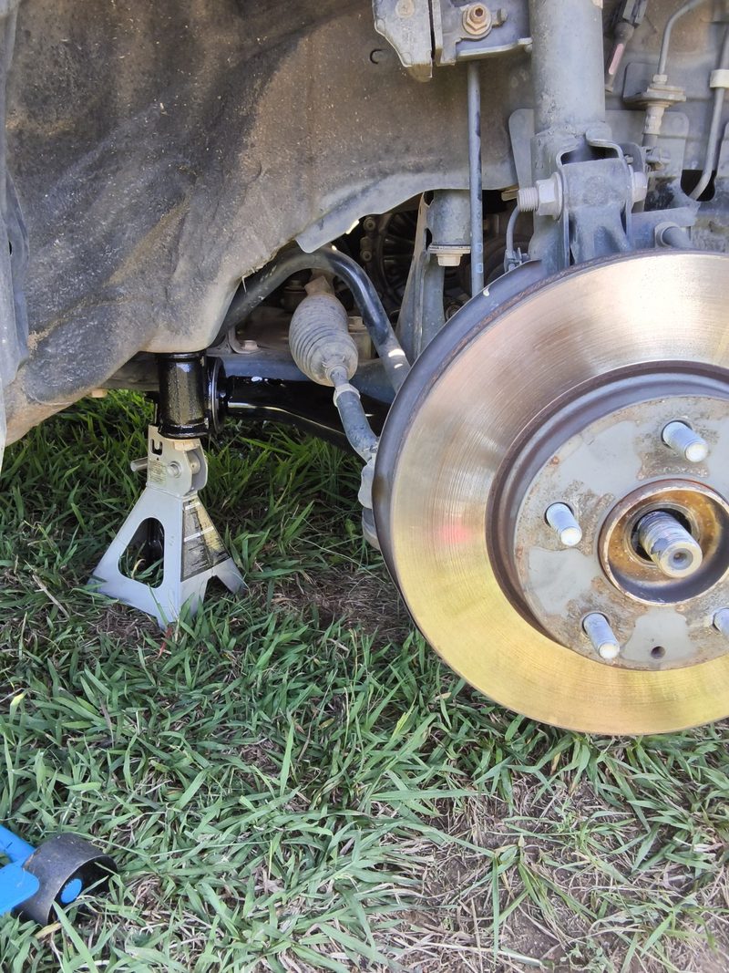 The front corner of the Mazda 3 on a jack stand with the wheel off and the rotor showing