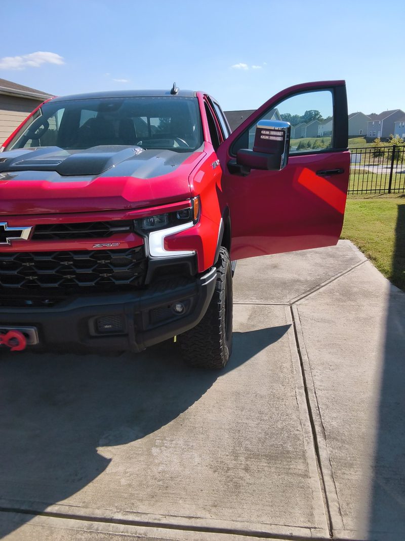 The red Silverado 1500 on the driveway with the driver door open after the battery swap