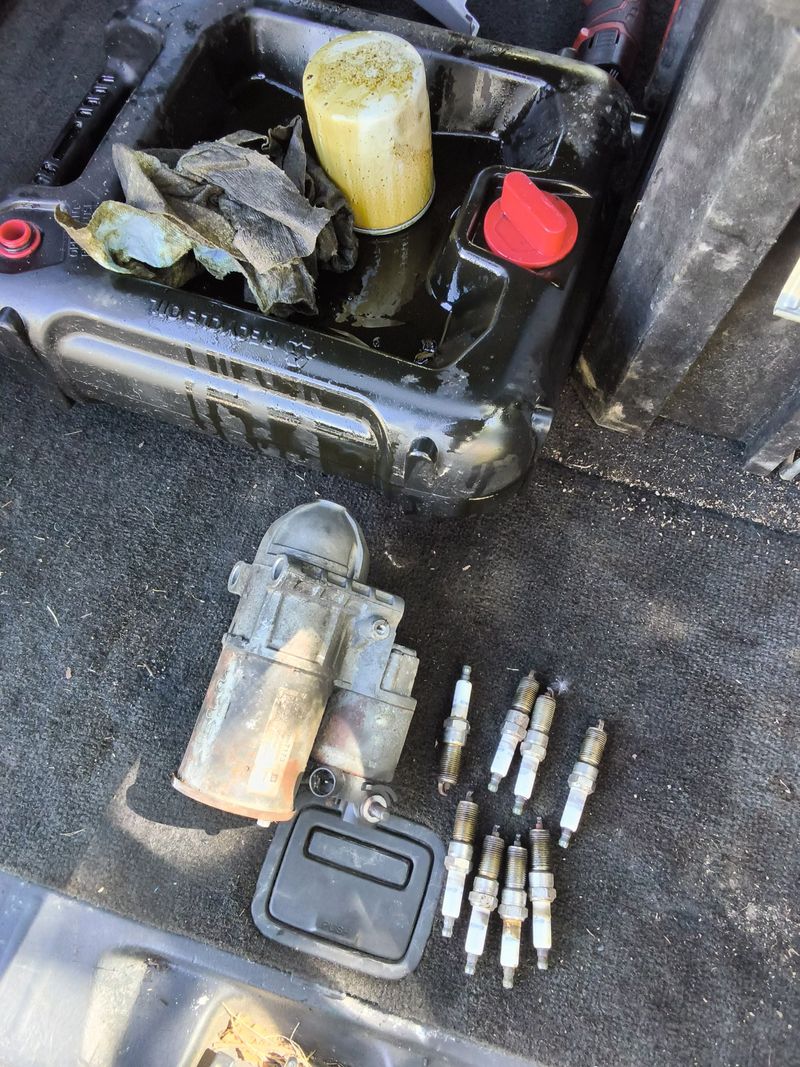 The old starter motor and a row of used spark plugs on a mat