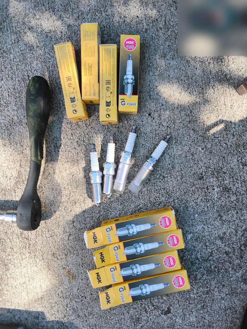 New NGK spark plugs and their boxes laid out next to a ratchet