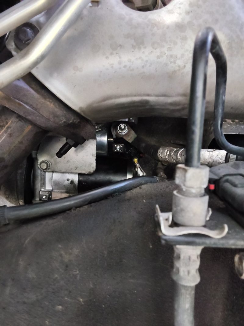 The new starter motor bolted in low on the engine of a Chevy Tahoe, seen from under the truck