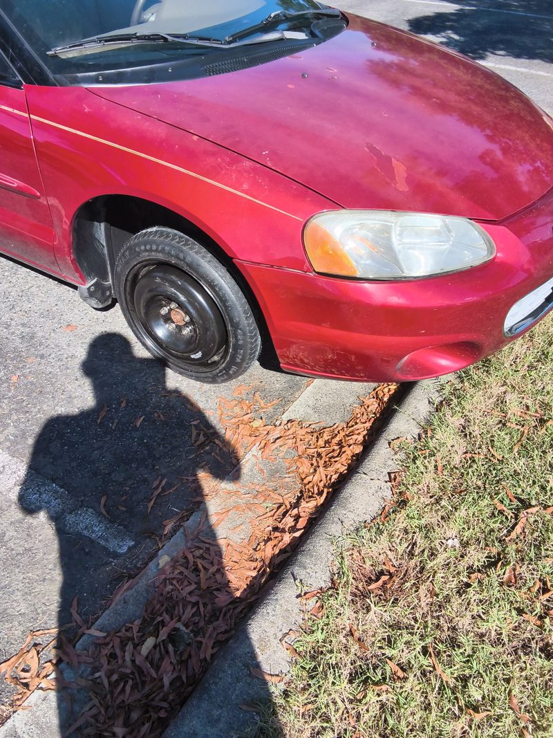Close view of the black spare wheel on the front of the red Sebring by a curb